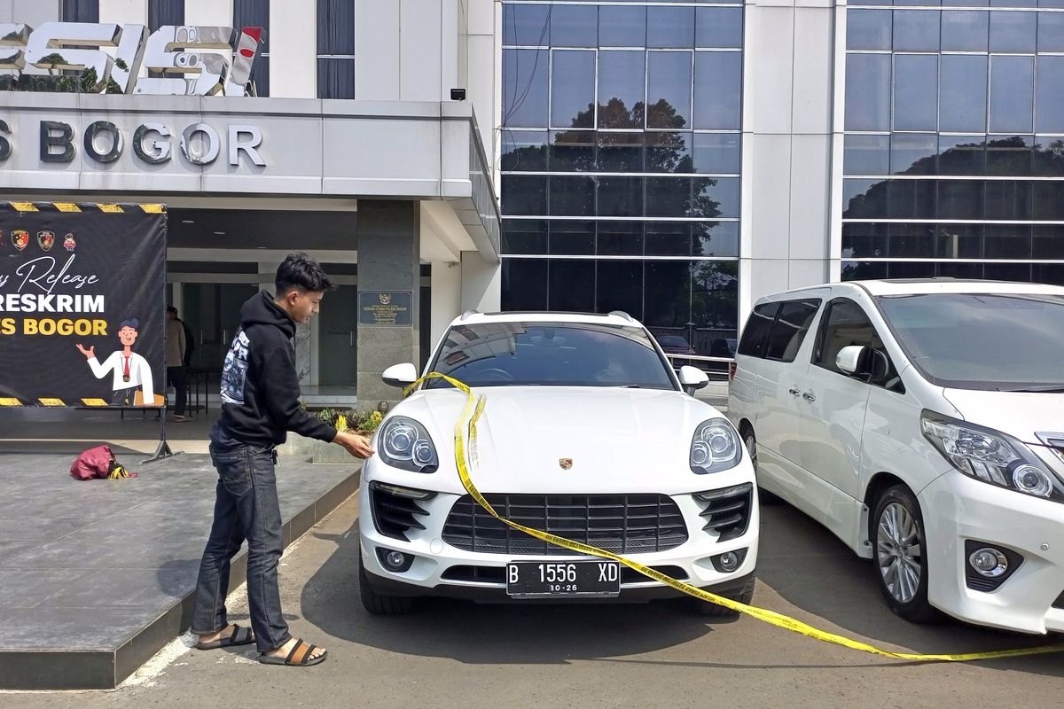 Anggota Reskrim Polres Bogor memasang garis polisi dalam barang bukti dua mobil mewah yang disita dari pelaku pemerasan pejabat Pemkab Bogor. Kini, dua mobil itu berada di halaman Polres Bogor, Jumat (26/7/2024).