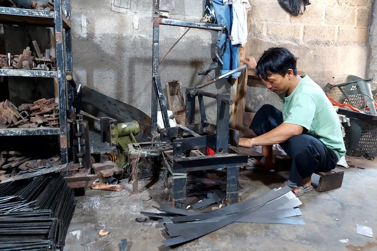 Anwarudin sedang memotong plat besi yang digunakan untuk membuat rak toko