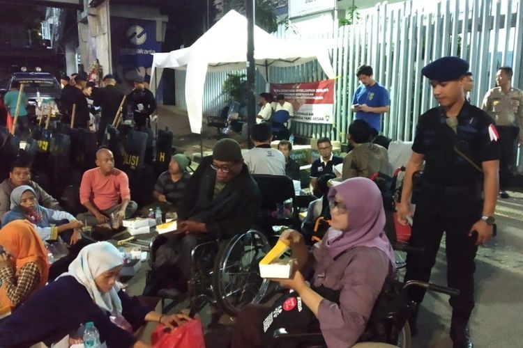 Tampak Brimob Mabes Polri bersama pasukan TNI dan komunitas penyandang disabilitas buka puasa di atas aspal beralaskan kardus di depan Kantor Bawaslu RI, Jalan MH. Thamrin, Jakarta Pusat, Sabtu (25/5/2019).