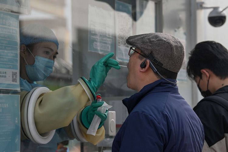 Petugas kesehatan mengambil sampel swab untuk tes Covid-19 dari seorang pria di stasiun pengumpulan asam nukleat di Beijing, China, Senin (25/10/2021). Penyebaran Covid-19 di China kembali menjadi peringatan setelah klaster baru terkait sekelompok wisatawan ditemukan 17 Oktober lalu.