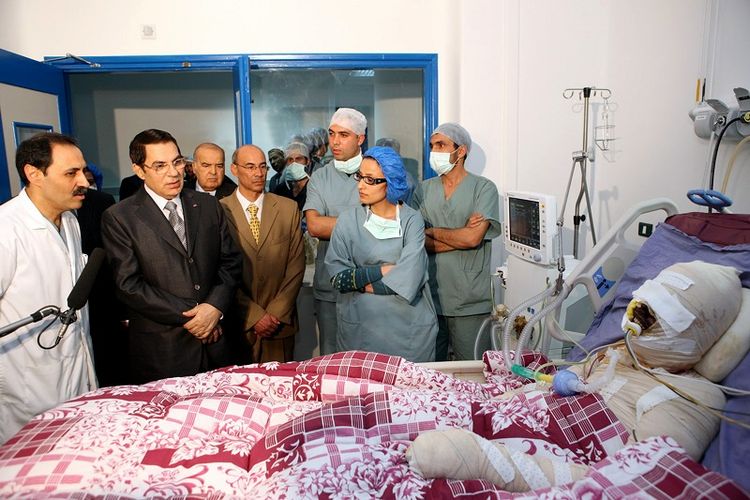 Foto yang dirilis oleh Kepresidenan Tunisia pada 28 Desember 2010 menunjukkan presiden Tunisia Zainal Abidin Ben Ali (kedua dari kiri, memakai jas hitam) mengunjungi Mohammed Bouazizi (kanan, yang terbalut kain perban), seorang pria berusia 26 tahun yang membakar dirinya, di Ben Arous dekat Tunis.