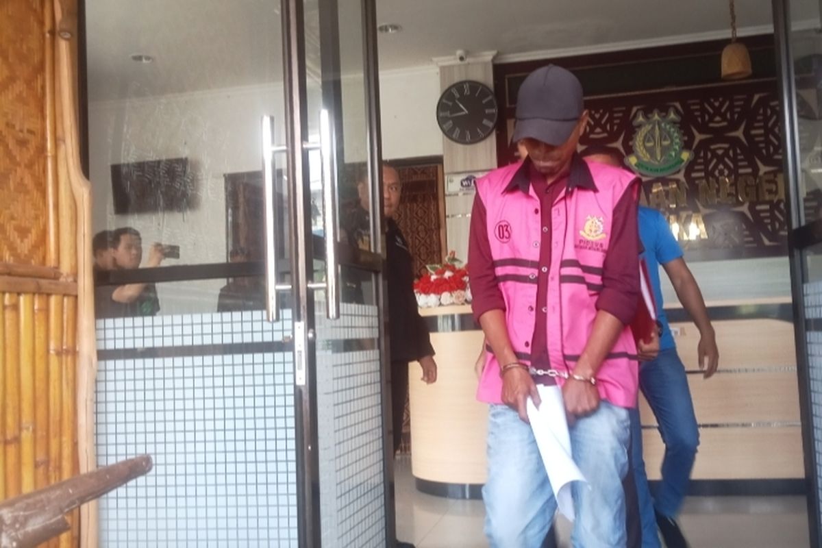 Tersangka YM mengenakan rompi tahanan dengan tangan diborgol saat menuju mobil tahanan di halaman Kantor Kejaksaan Negeri Sikka pada Senin (27/10/2025) 