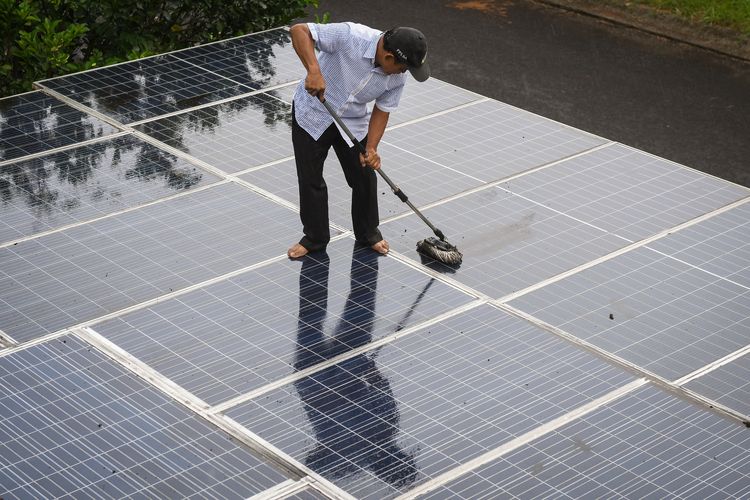 Yohanes Bambang Sumaryo membersihkan panel-panel surya yang terpasang pada atap rumahnya di Sawangan, Kota Depok, Jawa Barat.