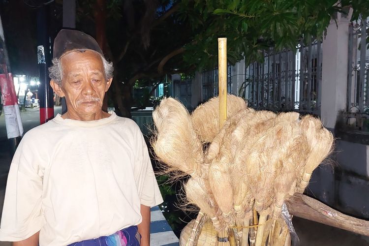 Dulrasu (73) bersama pikulan berisi sapu ijuk yang dia ajakan dengan cara berjalan kaki. Usaha ini sudah bertahun-tahun dijalani di wilayah Sumenep, Madura. Meski usianya sudah senja, dia pernah tidak ingin merepotkan kerabat bahkan kedua anak kandungnya, dia tetap gigih berusaha untuk hidupnya.

