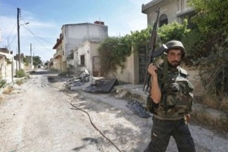 Seorang prajurit Suriah berpatroli sambil menenteng senjata di salah satu sudut kota Qusayr. Selama dua tahun konflik bersenjata di Suriah, sudah lebih 100.000 orang tewas.