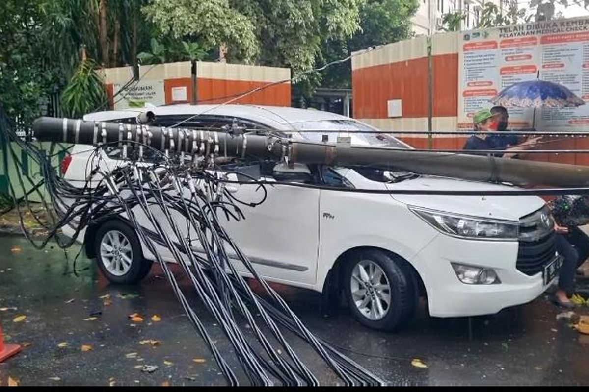 Hujan deras disertai angin kencang mengakibatkan satu tiang listrik tumbang dan menimpa mobil yang berada disekitarnya di Cempaka Putih, Jakarta Pusat, Rabu (23/3/2022).
