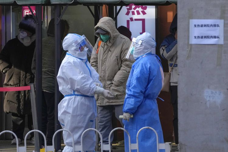 Petugas medis berbaju pelindung saling mengobrol saat warga menunggu masuk ke klinik demam sebuah rumah sakit di Beijing, Selasa, 13 Desember 2022.