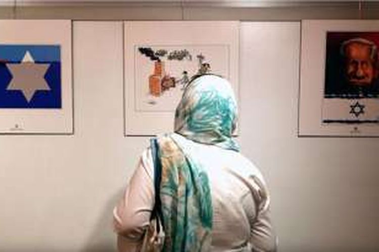 Wanita warga Iran sedang menikmati karya kartun dalam eksibisi international Holocaust II di Teheran 