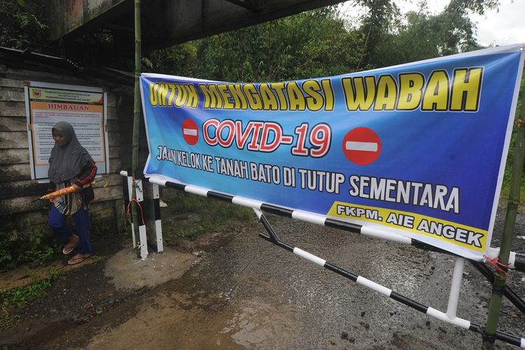 Warga melintas di samping portal yang menutup akses ke desa di Nagari Aia Angek, Kabupaten Tanah Datar,  Sumatera Barat, Jumat (17/04/2020). Warga menutup sejumlah akses masuk ke desa di daerah itu bagi pendatang untuk mencegah penyebaran COVID-19. ANTARA FOTO/Iggoy el Fitra/wsj.
