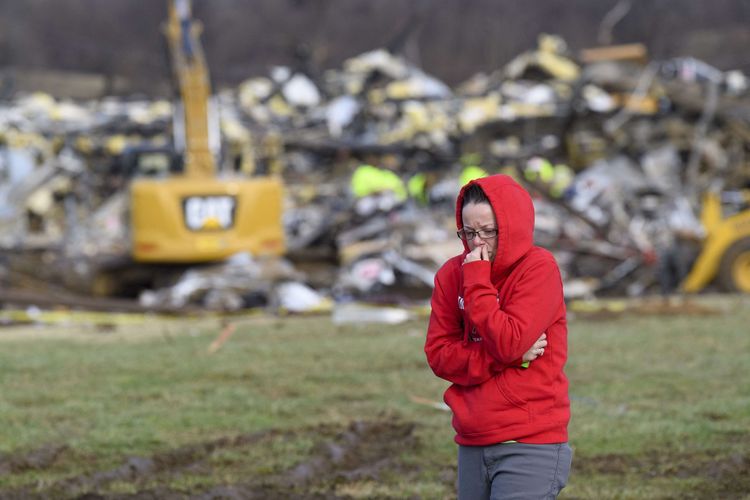 Seorang wanita berjalan dengan latar belakang puing-puing bangunan Pabrik Lilin Produk Konsumen Mayfield yang hancur setelah hantaman tornado di Mayfield, Kentucky, Amerika Serikat (AS), Sabtu (11/12/2021). Sedikitnya 70 orang dilaporkan tewas setelah tornado yang diduga terkuat sepanjang sejarah di Kentucky melanda sejumlah negara bagian AS dan menghancurkan banyak bangunan.