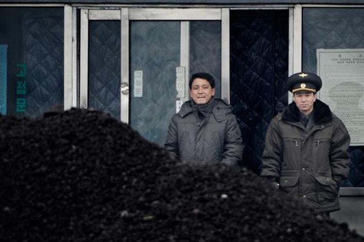 Seorang perwira militer dan seorang pria Korea Utara tengah mengawasi tumpukan batu bara di Sungai Yalu yang menjadi batas negeri itu dengan China.