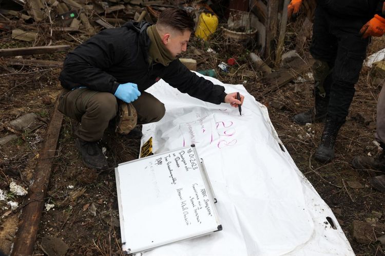 Seorang sukarelawan Ukraina menulis keterangan pada spanduk yang membawa jenazah tentara Rusia yang mereka gali di desa Dolina, wilayah Donetsk, pada 18 Januari 2023. 