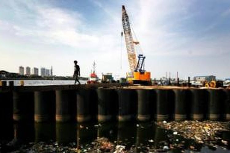 Warga melintas di antara dinding tabung raksasa yang dipasang sebagai bagian dari proyek pembangunan tanggul laut raksasa di Jakarta Utara, November 2014. 