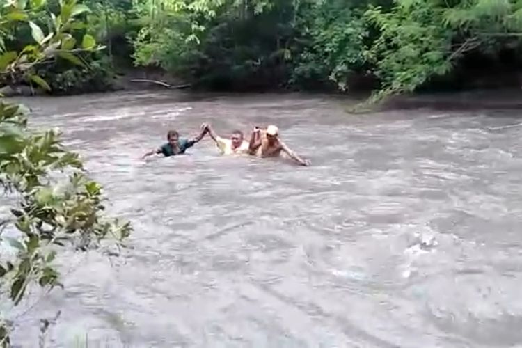 Tampak Pelaksana Tugas Kepala Sekolah Dasar Negeri Lumbung, Fransiskus Xaverius Geroda (tengah) dibantu oleh dua orang warga saat hendak menyeberangi Kali Maidang, Desa Maidang, Kecamatan Kambata Mapambuhang, Kabupaten Sumba Timur, Nusa Tenggara Timur (NTT), Kamis (28/1/2021) siang.