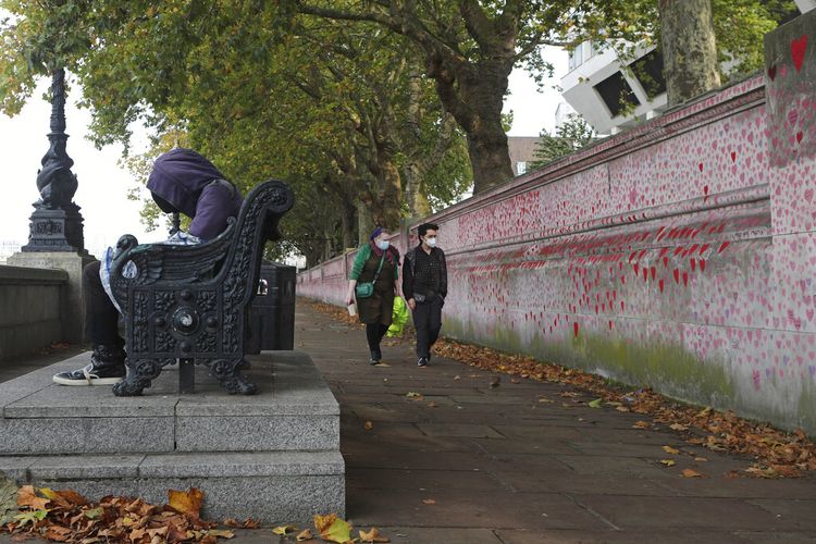 Seorang tunawisma beristirahat di bangku dekat National Covid-19 Memorial Wall di South Bank di depan Rumah Sakit St Thomas di London Selasa 19 Oktober 2021. 