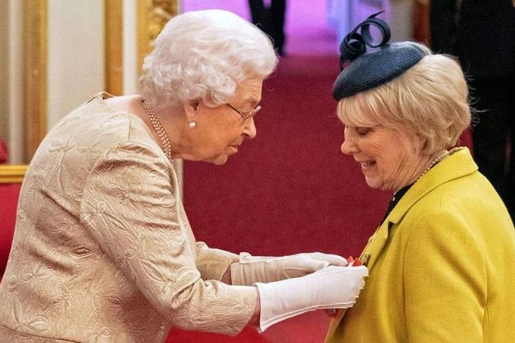 Ratu Elizabeth II memakai sarung tangan saat menyematkan medali pada upacara penobatan di Istana Buckingham, Selasa 3 Maret 2020.