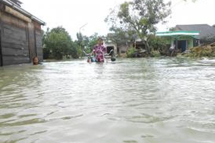 Seorang warga melintasi jalan yang tergenang banjir di Desa sayung sambil menuntun sepedanya,Senin (20/1/2014)