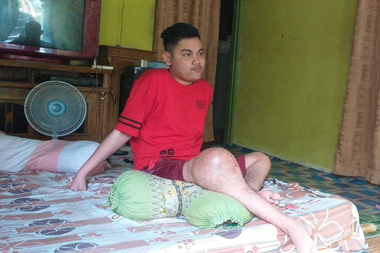 Marwan Alfidri (17), remaja yang mengidap tumor di kaki sebelah kakan sedang duduk di kasur ditemani ibunya, Siti Mariam, di ruang tengah rumahnya di Desa Pulau Jambu, Kecamatan Kampa, Kabupaten Kampar, Riau, Rabu (5/2/2020).