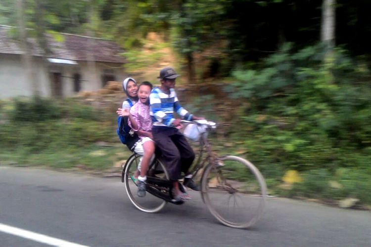 Hernowo mengendalikan kemudi sepeda, Kamilah dan Wahyu di belakang. Seperti inilah setiap hari Hernowo membawa Wahyu sekolah yang jauhnya belasan kilometer. Hernowo yang setengah tuli sejak lahir tidak menyerah menyekolahkan anaknya yang down syndrome. Di usia senja mereka, ia mengharapkan Wahyu bisa cepat mandiri.