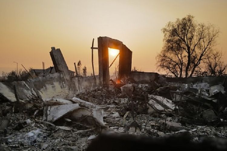Matahari terbenam dalam kepulan asap jauh di balik puing bangunan rumah-rumah akibat kebakaran di kawasan Fountaingrove di Santa Rosa, California, AS.