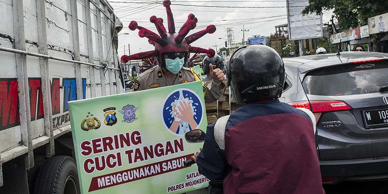 Anggota polisi memakai helm berbentuk virus corona melakukan imbauan dan penyemprotan cairan disinfektan pada kendaraan di jalanan di daerah Mojokerto, Jawa Timur, Jumat (3/4/2020). Cara unik ini dilakukan oleh sejumlah anggota dari Polres Mojokerto dalam upaya menekan penyebaran virus corona atau penyakit Covid-19 yang tengah merebak di Tanah Air.