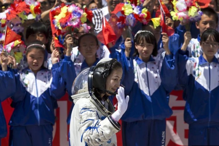 Pelajar China melambaikan bunga dan bendera nasional saat astronot perempuan Wang Yaping meninggalkan pusat peluncuran satelit Jiuquan menuju lokasi peluncuran, dekat Jiuquan, China barat, Selasa, 11 Juni 2013.