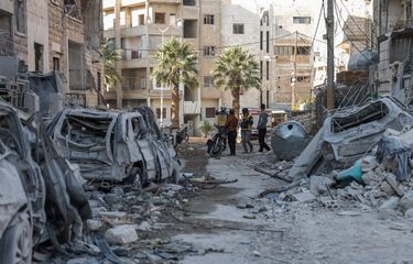Orang-orang dan penyelamat Suriah yang dikenal sebagai White Helmets berdiri di dekat puing-puing bangunan di lokasi serangan udara yang dilaporkan di sebuah lingkungan di kota utara Idlib yang dikuasai pemberontak Suriah pada 2 Desember 2024.