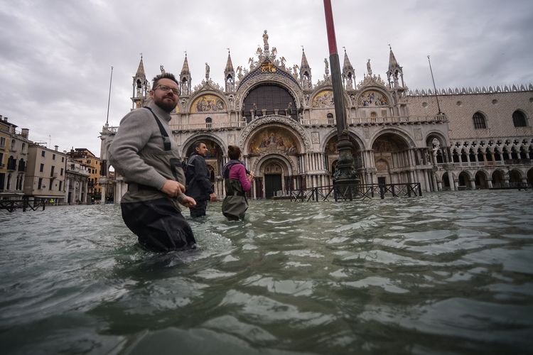 Sekelompok orang melewati Lapangan St Mark, dengan Basilika St Mark di depannya apda 15 November 2019. Venesia dihantam gelombang pasang tertinggi dalam 50 tahun terakhir, dengan pemerintah Italia mengumumkan keadaan darurat.