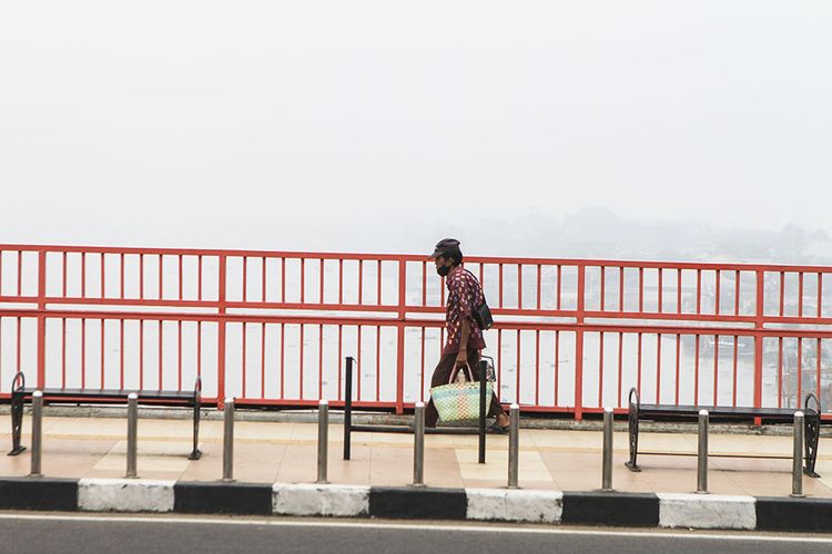 Seorang pedagang melintas di atas Jembatan Ampera Palembang, Sumatera Selatan, yang diselimuti kabut tebal, Selasa (28/9/2021). Berdasarkan laporan dari BMKG Sumatera Selatan, kabut ini disebabkan karena adanya perbuahan cuaca atau yang disebut dengan kabut adveksi.