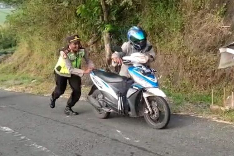 Ilustrasi tanjakan. Polisi  tengah mendorong sepeda motor yang tidak kuat melewati tanjakan ekstrem.