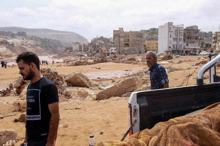 Orang-orang berjalan melewati mayat korban banjir bandang Libya di belakang truk pikap di Derna, 11 September 2023. Banjir di Libya timur menewaskan lebih dari 5.200 orang di kota pesisir Mediterania, Derna.