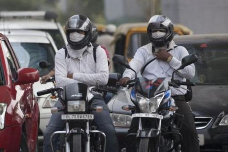 Pengendara motor menggunakan masker saat mengendarai kendaraannya melintasi jalanan kota New Delhi, India.