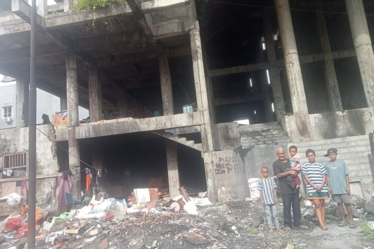 Yorgen Ayomi, saat mengendong cucunya, saat berdiri borsama beberapa anaknya disebuah bangunan kosong yang ditempatinya selama lima tahin berada di kawasan Kali Hanyaan, Kelurahan Entrop, Distrik Jayapura Selatan, Kota Jayapura, Papua, Minggu (20/7/2025).