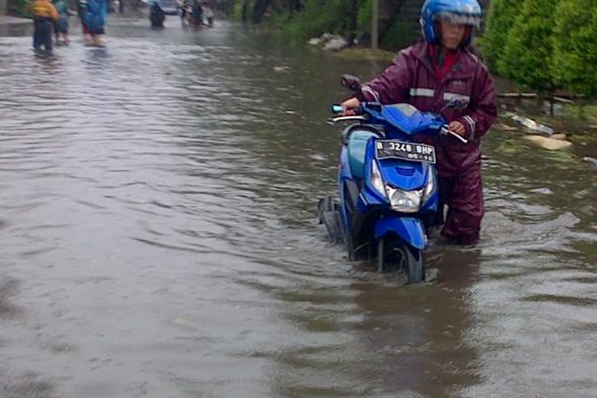 Salah satu pengendara terpaksa menuntun motornya lantaran banjir yang menggenangi jalan Peternakan II, Kapuk, Jakarta Barat, Senin (9/2/2015)