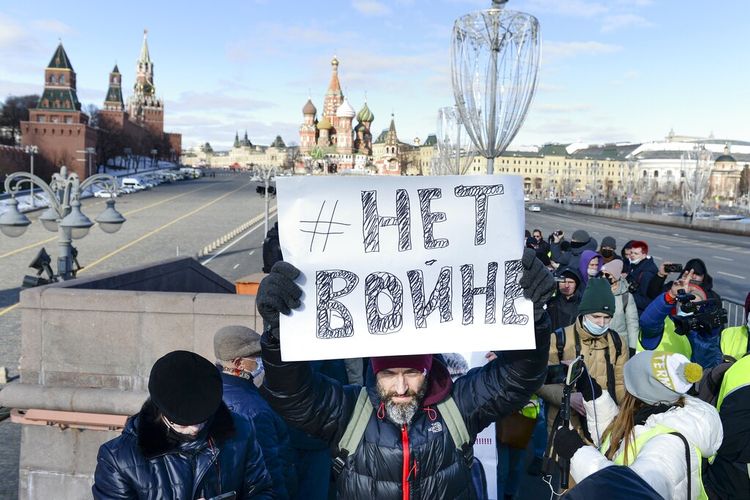 Seorang pria memegang poster bertuliskan No War ketika orang-orang meletakkan bunga di dekat tempat pemimpin oposisi Rusia Boris Nemtsov ditembak mati, dengan latar belakang Kremlin, (kiri) Menara Spaskaya (kedua dari kiri), dan St. Basil (tengah) di Moskwa, Rusia, Minggu (27/2/2022).