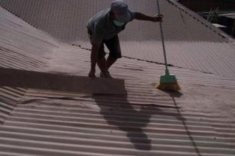 Warga membersihkan atap rumah dari debu letusan Gunung Sinabung di Karo, Sumatera Utara, Kamis (9/10/2014). Letusan gunung ini telah menewaskan 17 orang.