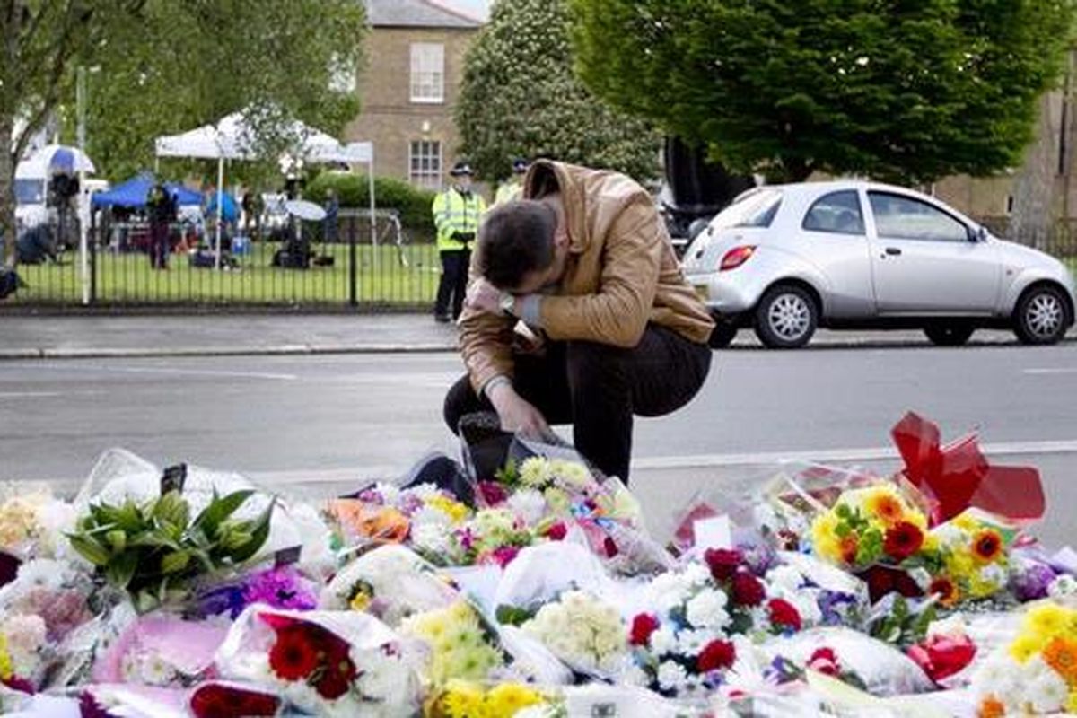 Seorang pria berdoa di depan tumpukan karangan bunga di luar barak Woolwich, London.