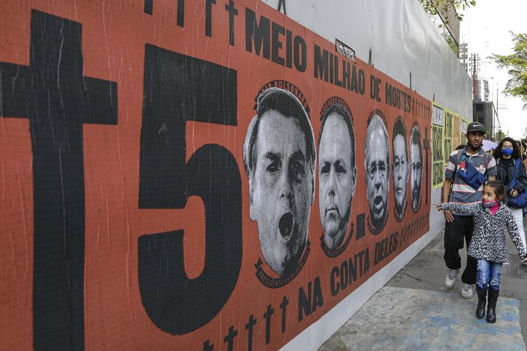 Seorang gadis menunjuk mural yang menampilkan wajah Presiden Brasil Jair Bolsonaro saat memprotes penanganannya terhadap pandemi Covid-19 di sepanjang Paulista Avenue, di Sao Paulo, Brasil, Sabtu, 19 Juni 2021. 