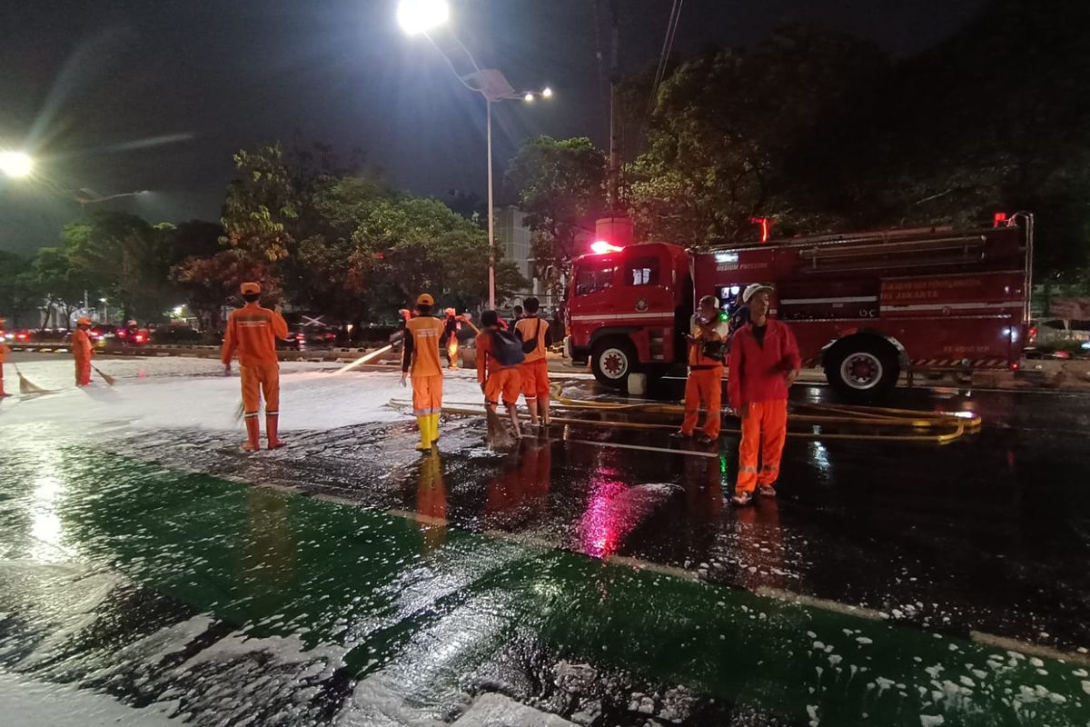Sudin Damkar Jakarta Timur membersihkan tumpahan oli yang menjadi penyebab pengendara sepeda motor tewas di tempat akibat tergelincir dan terlindas di Jalan Matraman, Kebon Manggis, Matraman, Jakarta Timur, Senin (5/6/2023) malam.