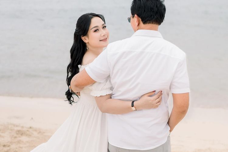 Puput Nastiti Devi tampil anggun dengan long dress putih, makeup natural, dan rambut wavy saat foto kehamilan anak ketiga bersama keluarga.