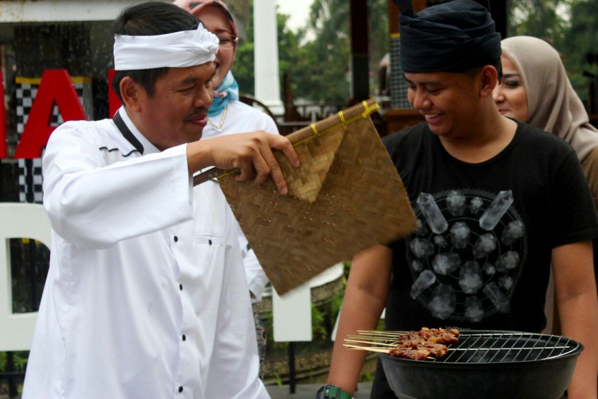 Bupati Purwakarta Dedi Mulyadi (kiri, baju putih), berbincang dengan salah satu warganya sembari mengipasi bakaran sate