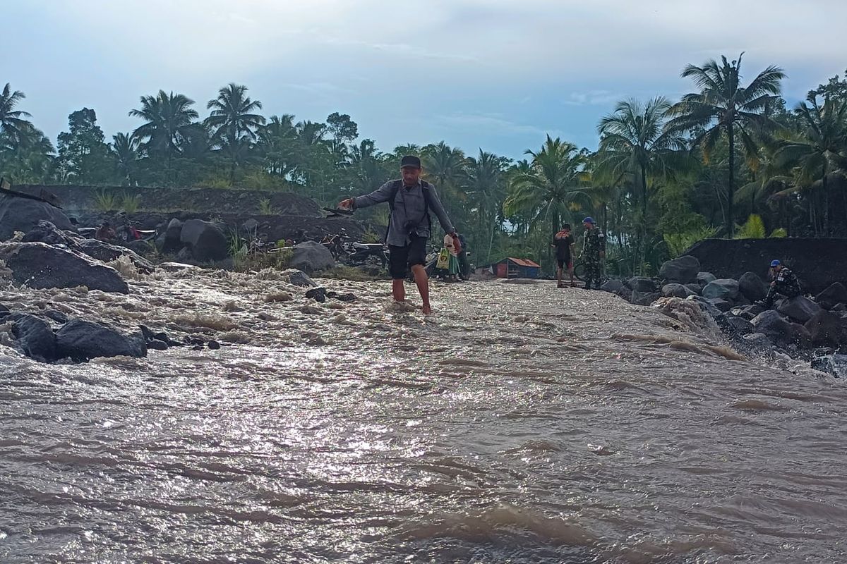 Warga melintasi sisa banjir lahar hujan Gunung Semeru di Sungai Regoyo, Sabtu (28/6/2025)