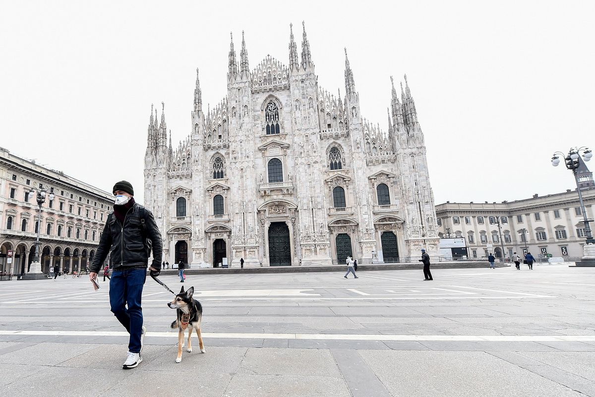 Seorang pria memakai masker berjalan dengan anjingnya di Duomo Square, Milan, Italia. Kebijakan karantina diterapkan di seluruh Italia mulai 10 Maret sampai 3 April 2020.