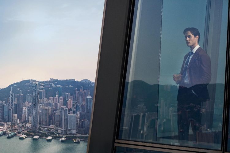 Seorang investor memandang cakrawala kota Hong Kong dari balik jendela gedung pencakar langit. Stabilitas hukum, pajak ringan, dan ekosistem keuangan kelas dunia menjadikan Hong Kong destinasi favorit para miliarder global untuk mendirikan family office.