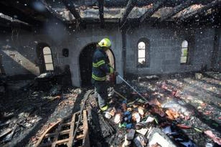 Seorang anggota pasukan pemadam kebakaran menyemprotkan air untuk memadamkan api yang menganguskan salah satu bangunan di dalam sebuah kompleks gereja di Tabgha, Israel.