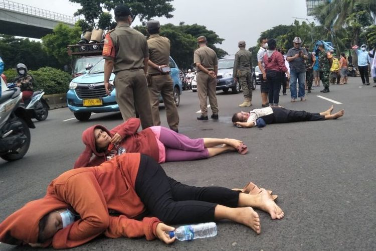 Pedagang Kaki Lima (PKL) tiduran di jalan sebagai bentuk protes terkait penertiban yang dilakukan petugas di depan Rumah Sakit Umum Universitas Kristen Indonesia (UKI), Jakarta Timur, Selasa (18/1/2022).