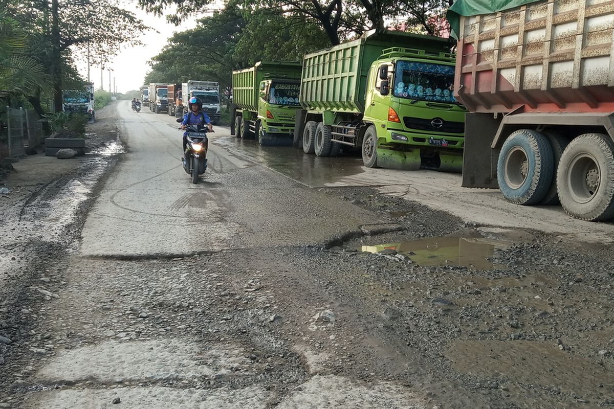 Seorang pengendara melintas di samping truk tronton angkutan tambang yang berhenti untuk melanjutkan perjalanannya dari arah Jalan Sudamanik menuju perbatasan jalan raya Parung Panjang, Bogor menuju Legok, Kabupaten Tangerang, Banten, Sabtu (18/1/2020).