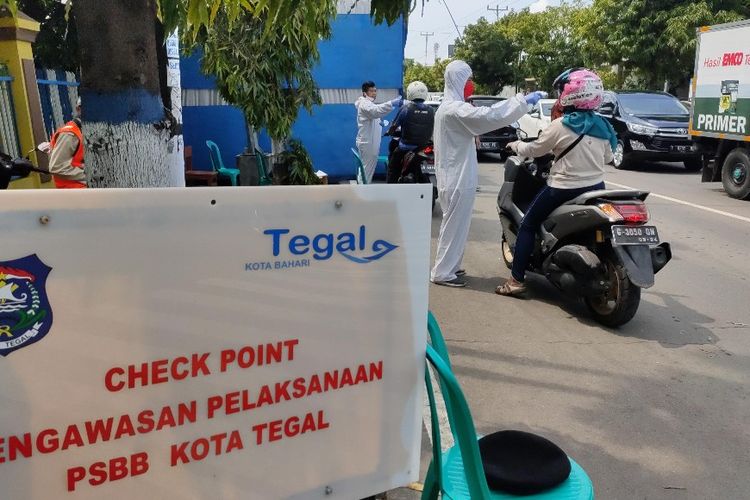Petugas medis mengenakan alat pelindung diri mengecek suhu tubuh pengendara sepeda motor yang akan masuk ke dalam Kota Tegal, Jawa Tengah di depan posko check point Jalan Proklamasi dalam masa penerapan pembatasan sosial berskala besar (PSBB), Senin (4/5/2020)