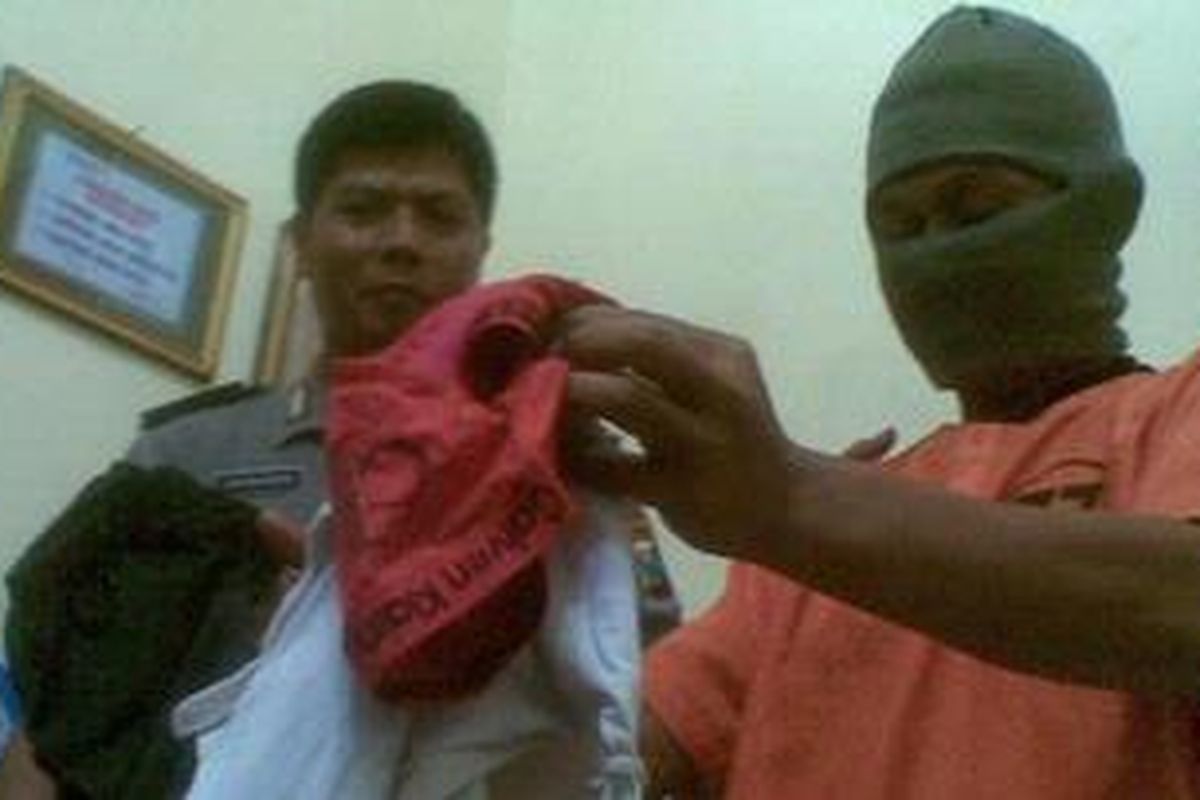 Tersangka Yomi Paulus (bertutup muka) menunjukkan barang bukti berupa baju korban, saat gelar perkara di Mapolres Kediri Kota, Senin (16/5/2011)  