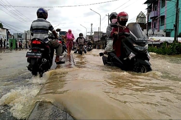 Seorang warga mendorong sepeda motor yang mogok saat melintasi banjir di Desa Lalang, Kecamatan Sunggal, Deli Serdang pada Jumat (4/12/2020).